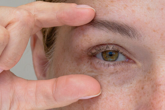 Eye with slightly hooded eyelid, accentuated by fingers gently framing the brow and lower eyelid