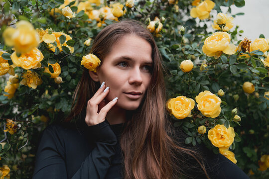 Young woman posing beside vibrant yellow rose bush outdoors in natural light