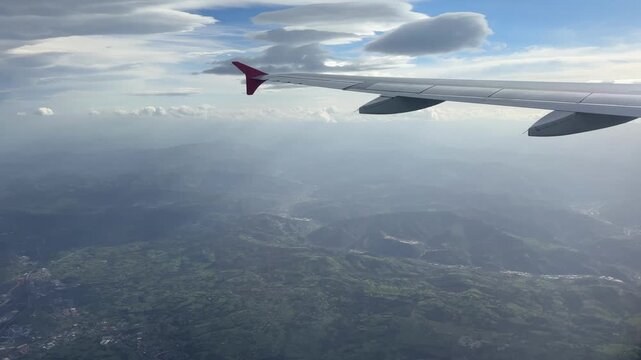 Aerial view from an airplane window showcasing a magnificent cloudscape above rolling green mountains, valleys, and countryside during a peaceful flight journey, perfect for travel and aviation stock