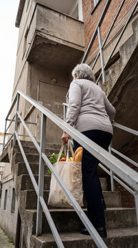 Senior woman carrying grocery bag up exterior apartment stairs, authentic active aging concept showing independence confidence value value value value value value value value value