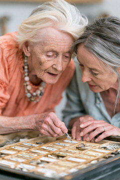 Elderly women labeling jewelry box compartments with daughter's help