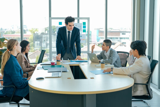 Business manager leans over table to discuss strategy with colleagues. Team reviews ideas, analyzes business goals, solves problems, strengthens collaboration, planning, organizational growth.