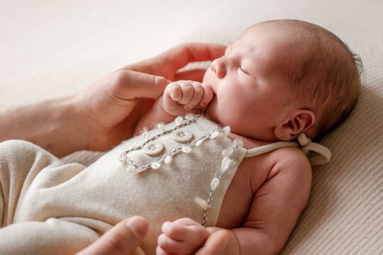 Peaceful newborn baby sleeps soundly, adult hand gently resting near its head on soft fabric.