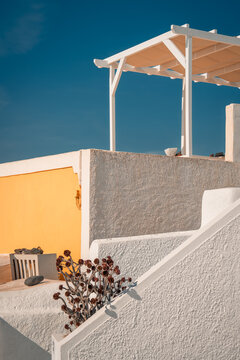 Minimalist cycladic architecture featuring a pergola, white steps, and a vibrant yellow wall under blue sky
