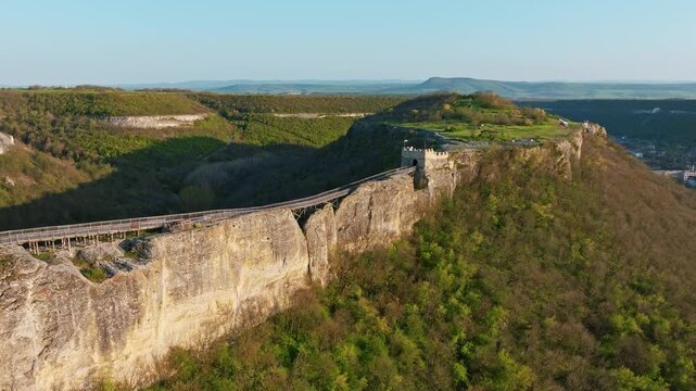 Panoramic aerial view of Ovech Fortress standing on a high rock plateau in Provadia, Bulgaria, with a long wooden bridge connecting the medieval cliff walls