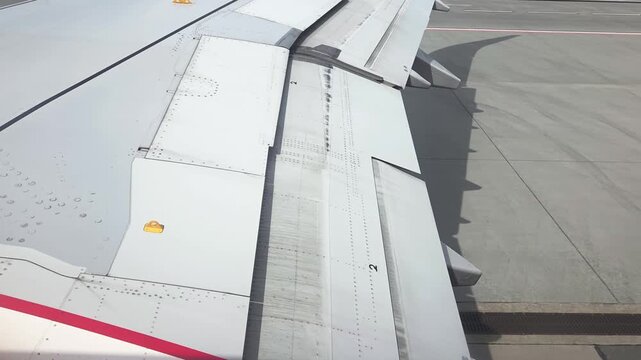Aircraft wing flaps in transition during taxiing on runway, showcasing detailed wing structure and markings, with airport tarmac visible in the background