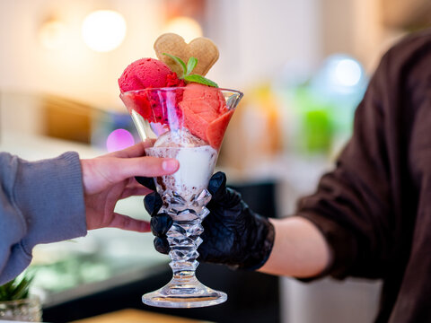 Customer receives vibrant strawberry ice cream parfait from gloved server.