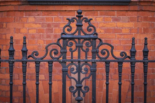 Black, ornate wrought iron fence in front of a brown-red brick wall, Chelsea, London, England, Great Britain