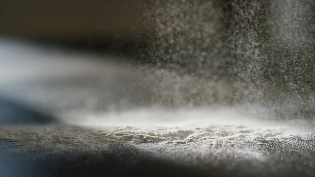 White flour falling and dusting dark table surface while sifting during baking process in kitchen