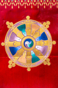 Norbulingka Institute, Sidhpur, Himachal Pradesh, India. An artistic depiction of the Dharmachakra, the Buddhist wheel of law, on a red background adorned with gold motifs.
