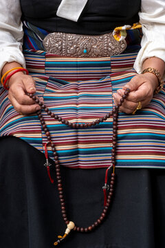 Hands holding a traditional Buddhist rosary, adorned with bracelets and a silver belt, in Dharamsala, Himachal Pradesh, India.
