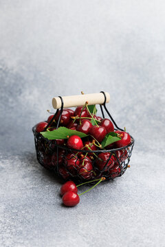 Fresh cherries placed in a small wire basket on a gray surface during daylight hours