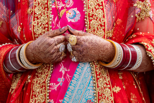 An Indian bride's hands, decorated with henna, wearing traditional bracelets and jewelry during a wedding ceremony. Chandreshwar, Himachal Pradesh.