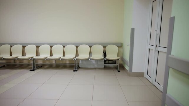 Empty medical corridor features rolling gurney table and row of plastic waiting chairs. Quiet clinical setup feels sterile and spacious