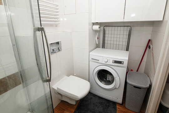 Modern small white bathroom with built-in washing machine and toilet. Compact apartment laundry space, minimalist bathroom design, functional home interior layout, space-saving renovation