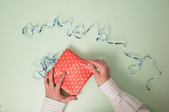 Gift unwrapping: A hand tears away the wrapping paper from a gift. Top view of a red polka dot present on a mint green background
