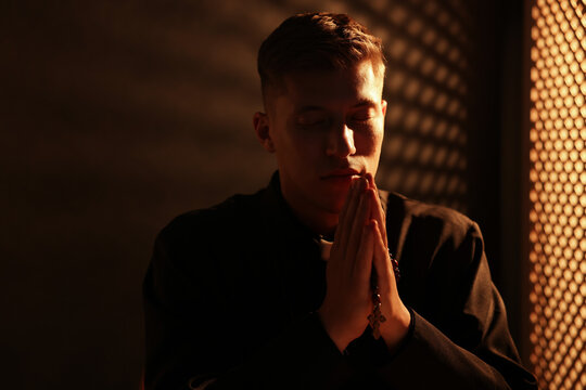 Priest with rosary praying in confessional booth. Space for text