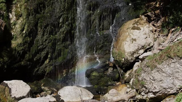 Static shot of Wasserlochklamm waterfall with a bright rainbow in the water mist, Palfau, Austrian Alps