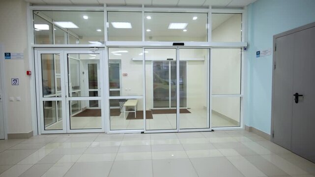 Spacious entrance lobby features large glass sliding doors and tiled glossy floor. Bright ceiling lighting creates welcoming atmosphere