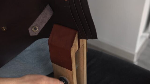 Leather craftsman using wooden clamp tool for creating handmade wallet in artisan workshop