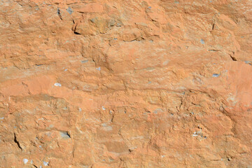 Fototapeta premium A detailed close up view shows the rough surface of a natural orange rock wall under bright daylight