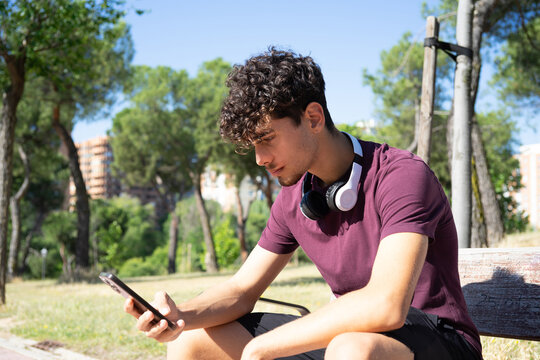Young person with headphones looking at their phone in the park
