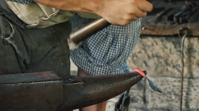 Blacksmith forging glowing red hot iron on anvil in traditional workshop for metal craft.