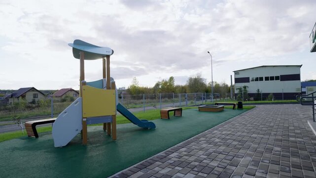 Spacious play yard features modern playground complex sandbox and wooden benches. Overcast daylight creates calm outdoor atmosphere