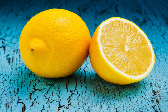 Lemon alongside cut half slice on blue wooden background