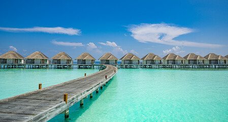 Fototapeta premium Maldives ocean overwater bungalows turquoise lagoon wooden jetty blue sky. Luxury tropical travel paradise honeymoon resort marketing. Sunny sky aqua clear water scenic wallpaper background design