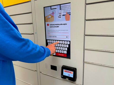 Person in blue sweatshirt using touchscreen to enter tracking number at modern automated parcel locker pickup station