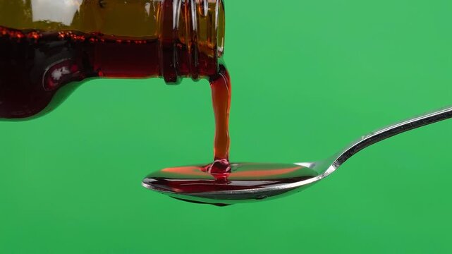 Close-up of red cough syrup pouring from brown bottle onto a metal spoon
