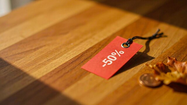 Red discount price tag on wooden table with autumn leaves and copy space