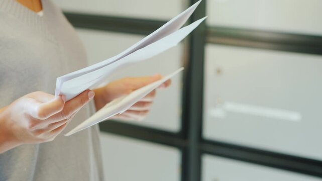 Close-up of woman hands holding and sorting through mail or documents near lockers.