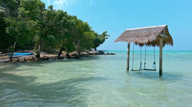 Scenic Barakuda Beach with a rustic wooden swing set over clear shallow turquoise water next to lush green trees, creating a relaxing holiday getaway scene in Karimunjawa, Indonesia RAW VIDEO