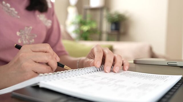 Woman Checking Expense And Inventory List In Notebook Beside Laptop, Personal Finance, Budget Planning, Bookkeeping, Small Business Accounting, Stock Management And Home Office Productivity
