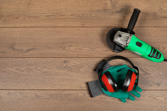 Angle Grinder with Protective Gloves and Hearing Protection on Wooden Background