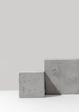 Vertical close-up of two concrete cube podiums arranged in a stepped overlapping formation against a light gray background, emphasizing cement texture and geometric structure for product display use.