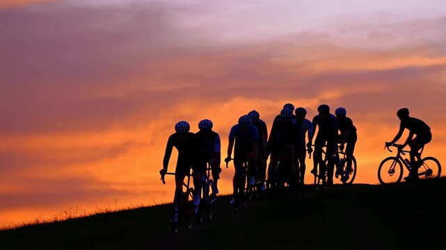 Silhouetted cycling group riding along grassy ridge at vibrant sunset, low viewpoint panoramic scene with warm cloudscape, strong backlight, expansive horizon, outdoor energy