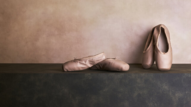 Professional pink satin ballet pointe shoes arranged on a dark rustic shelf against a soft neutral background, evoking feelings of dedication, grace, and classical dance.