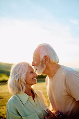 Happy senior couple bonding outdoors, enjoying a romantic moment together with a forehead kiss at...