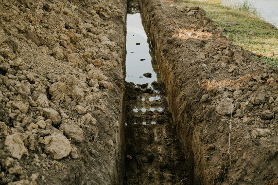 ditch with still water in natural outdoor setting, close-up perspective, brown soil and gray water, mood.