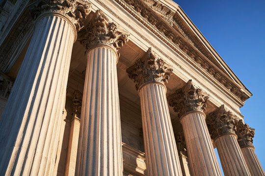 Low angle view of majestic neoclassical marble columns against a clear blue sky, representing justice, law, history, and government institutions in a professional and authoritative architectural
