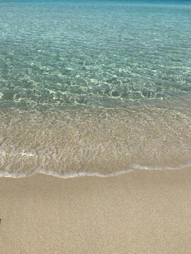 Crystal-clear turquoise seawater gently washing onto a golden sandy beach on Elafonisos Island, Greece. Peaceful Mediterranean shoreline with transparent water and soft waves, ideal for travel, summer