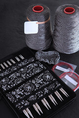 Obraz premium Knitting kit: set of interchangeable metal knitting needles in an organizer and bobbins with black-white yarn on dark background. An empty label for label