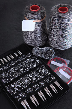 Knitting kit: set of interchangeable metal knitting needles in an organizer and bobbins with black-white yarn on dark background. An empty label for label