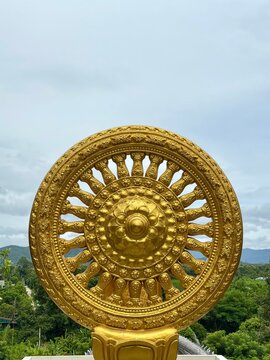 Golden Wheel of Dharma sculpture against a blue sky at a Buddhist temple in Thailand