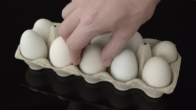 Hand selecting an egg from a cardboard carton on a black reflective surface