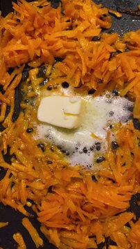 Grated carrots frying in a pan a pat of butter slowly melting and simmering preparing a healthy side dish.