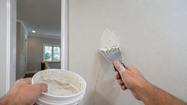 Handyman patching cracked plaster wall with putty knife